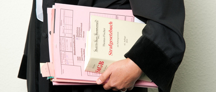 Eine Juristin in Robe trägt Strafakten und das Strafgesetzbuch unter dem Arm